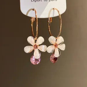 Macro detail of elegant flower hoop earrings featuring pink zirconia pendants.