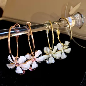 Detailed view of elegant gold hoop earrings featuring white resin flower pendants with crystals.