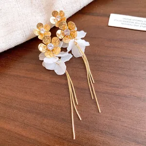 Détail des boucles d'oreilles fleurs dorées avec pétales en résine blanche et pompons.