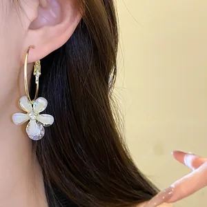 Close-up of elegant gold hoop earrings with white resin flower and sparkling zircon