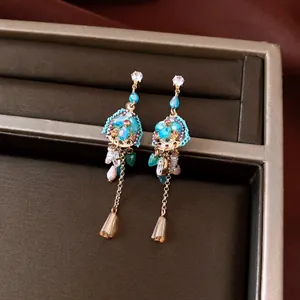Detalle de pendientes vintage con cuentas azules y largas cadenas doradas en caja