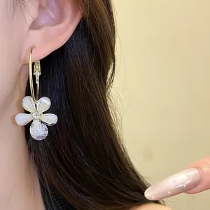 Close-up of elegant flower hoop earring with white petals and zircon center worn on ear