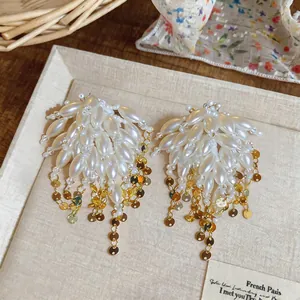 Detail shot of white pearl earrings with gold leaf tassels on a textured beige tray.
