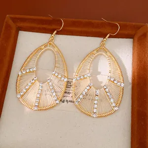 Gros plan de boucles d'oreilles goutte dorées avec fil de soie beige et strass brillants