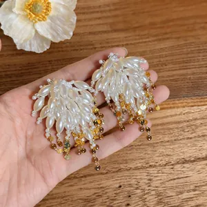 Elegant pearl tassel earrings with white pearls and golden sequins shown on hand