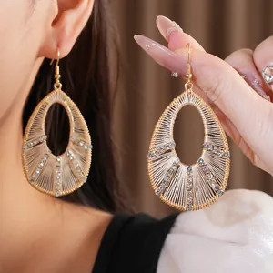 Vue détaillée de boucles d'oreilles dorées en forme de goutte avec strass et fils tissés.
