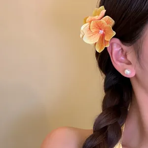 Detailed view of a warm orange flower hair clip worn by a model for a seaside vacation style.
