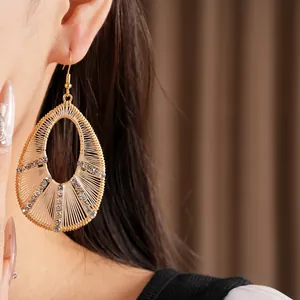 Détail de boucles d'oreilles dorées en forme de goutte avec tissage de fils et strass.