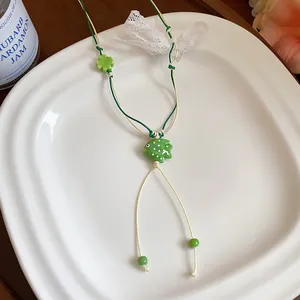 Detail view of a green ceramic fish necklace with polka dots on a white plate backdrop