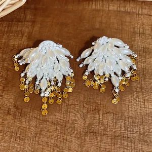 Detailed view of luxury pearl tassel earrings with gold sequins on a wooden background.