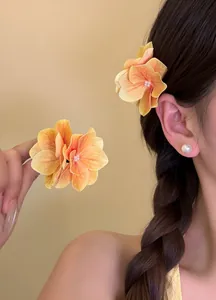Close-up detail of realistic orange hydrangea petal hair clip worn on braided hair with pearl earring