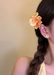 Detail view of an orange flower hair clip worn on a braided hairstyle for a vacation look
