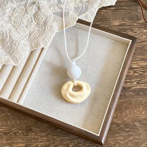 Close-up detail view of the pleated resin pendant on a minimalist white cord necklace.