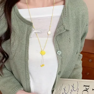 Detail of a handmade yellow ceramic fish necklace on a model's green cardigan