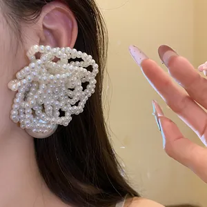 Close-up detail of a large white multi-layered pearl cluster flower earring on an ear.