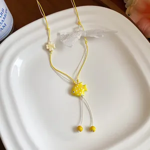 Close-up detail of yellow ceramic fish necklace with lace bow on a white plate