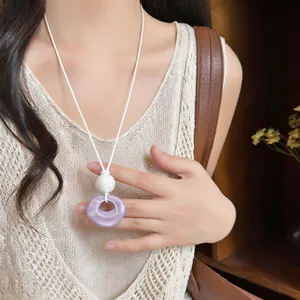 Close-up detail of purple resin donut pendant on white cord necklace worn by model