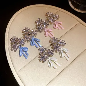 Sparkling zircon flower earrings with pastel bow accents displayed on jewelry pad