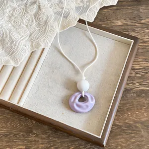 Macro view of a light purple round wrinkled resin pendant necklace on a white leather cord.