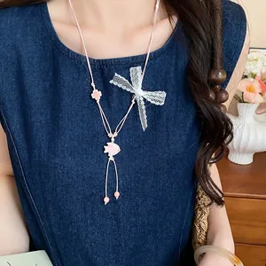 Exquisite pink cord necklace with ceramic fish and lace bow detail on denim dress