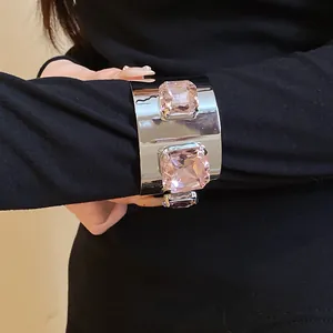Close-up view of a wide silver metallic cuff bracelet with two large pink square stones.