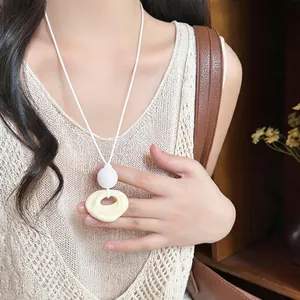 Detailed view of cream organic resin pendant necklace on beige knitted tank top