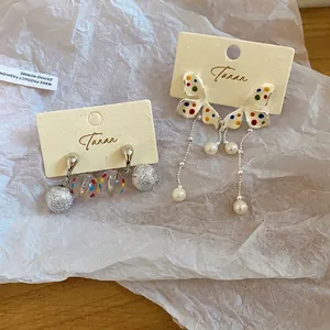 Orecchini a farfalla coreani con pois colorati e nappe di perle su carta bianca stropicciata.