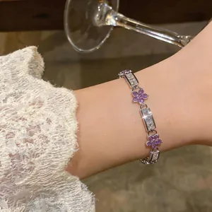 Detailed close-up of a silver bracelet with purple zircon flowers and lace sleeve background