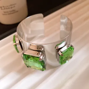 Close-up of a silver metal cuff bracelet featuring large square faceted green gemstones
