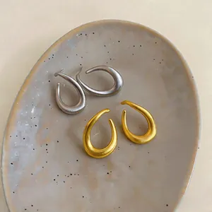 Detailed close-up of gold and silver minimalist twisted oval hoop earrings on a ceramic tray
