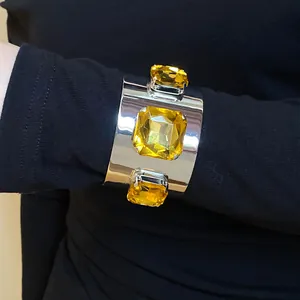 Detailed view of a silver-toned metal cuff bracelet with three yellow square gemstones.