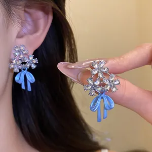 Detailed macro shot of silver needle flower earrings with blue enamel bow and zircons