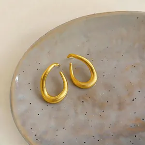 Detailed macro shot of minimalist gold twisted oval hoop earrings on a ceramic plate.