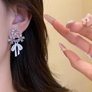 Close-up of elegant silver needle zircon flower earrings with a white bow pendant