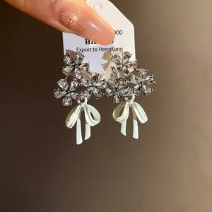 Close-up detail of silver needle zircon flower stud earrings with white oil-drop bows
