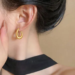 Detail shot of minimalist matte gold waterdrop earrings worn by a model.