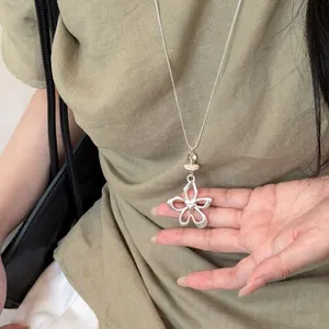 Dettaglio della collana con pendente a fiore e cuore in argento su fondo lino verde