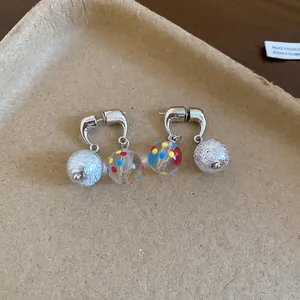 Dettaglio di orecchini stile coreano con pois colorati e perle argentate lucenti.