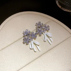 Close-up of elegant flower and white bow stud earrings with sparkling zircons