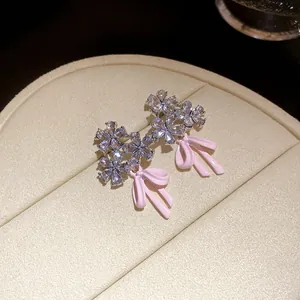 Close-up of elegant floral zircon stud earrings featuring pink enamel bow charms
