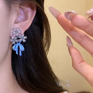 Close-up of zircon flower earrings with a light blue bow pendant worn on an ear.
