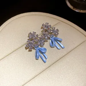 Detailed macro view of elegant zircon flower earrings with light blue enamel ribbon bows.