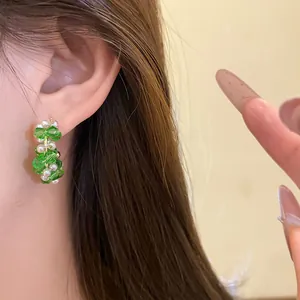 Elegant green beaded C-shaped stud earrings with white pearls shown on model's ear