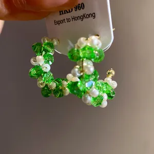 Close-up of handmade C-shaped earrings with green crystal beads and white pearls