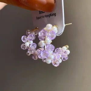 Close-up detail of C-shaped hoop earrings with purple glass beads and white pearls