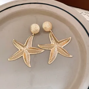 Macro view of vintage gold starfish drop earrings featuring a detailed textured surface