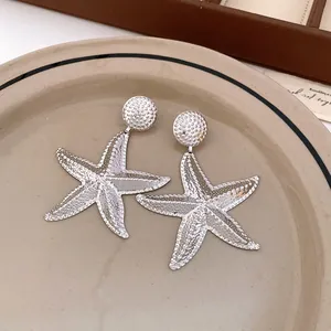 Close-up of silver textured starfish drop earrings on a vintage beige ceramic plate.