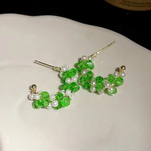Macro detail of green glass and pearl beaded C-shaped earrings with silver needle posts