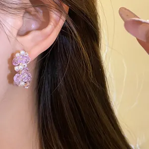 Close-up view of elegant purple glass bead and pearl C-shaped stud earring worn on ear