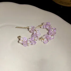 Detail of C-shaped earrings with purple glass beads and white pearls on gold wire.